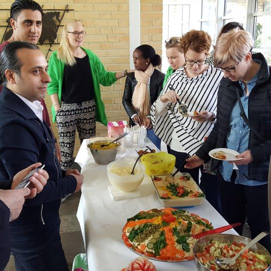 Bild från öppet hus där deltagare från etableringskursen står intill en buffet de förberett och en kö av hungriga besökare