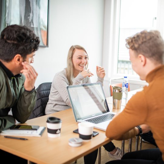 Tre deltagare grupparbete i klassrum med laptop